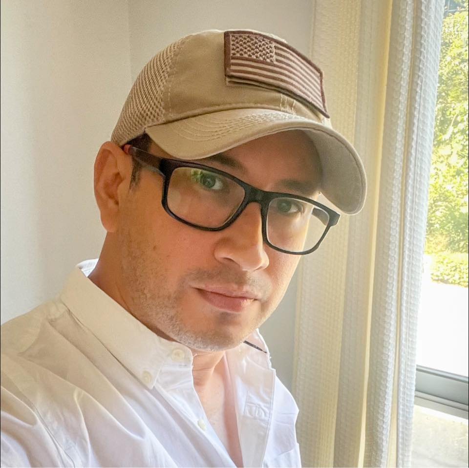 Retrato de Alek, fotógrafo de bodas caribeño, con gorra y camisa blanca junto a una ventana